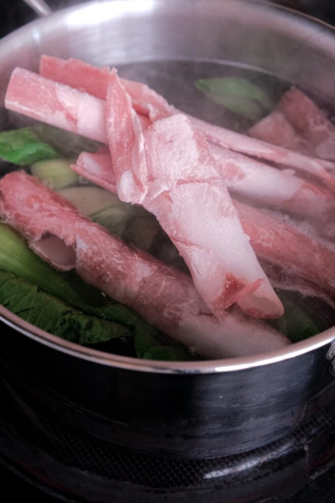 Boiling some sliced meat into the noodle soup.